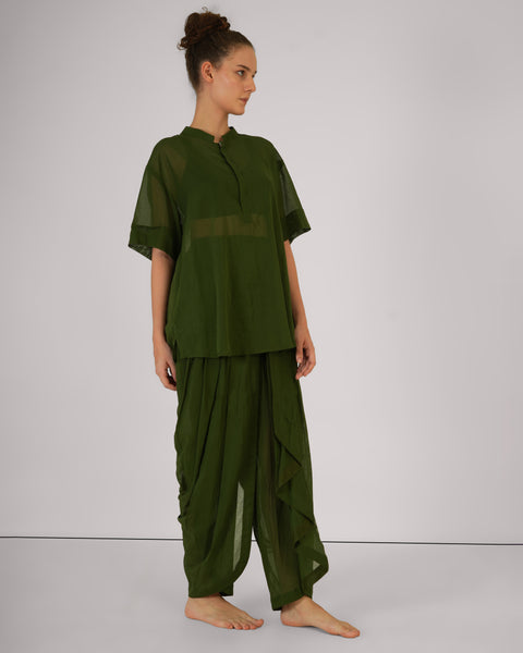 Female standing casually, side profile, wearing Mehndi green cotton yoga set, breathable natural fabric, white studio background.