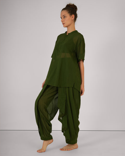 Female standing in relaxed stance, side view, in Mehndi green cotton yoga set, breathable natural fabric, white studio background.