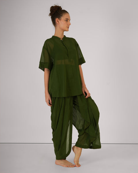 Female standing relaxed, side view, in Mehndi green cotton yoga set, breathable natural fabric, white studio background.