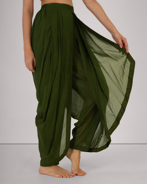 Female model holding side of Mehndi green 100% cotton yoga pants, demonstrating drape, breathable natural fabric, front view, white studio background.